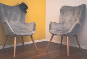 Two grey velvet chairs with a hat on one