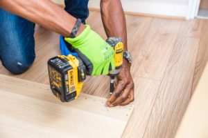 A man putting a nail into a wood floor using an electric screwdriver